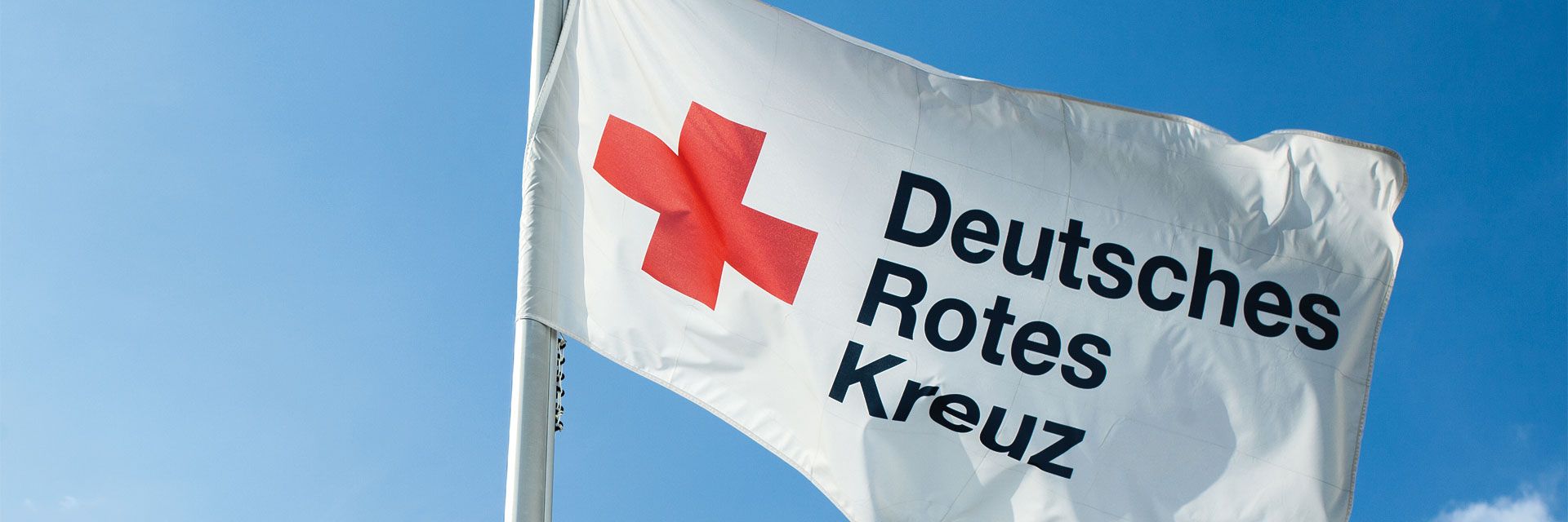 Bild: Eine Fahne des Deutschen Roten Kreuzes weht unter strahlend blauem Himmel.